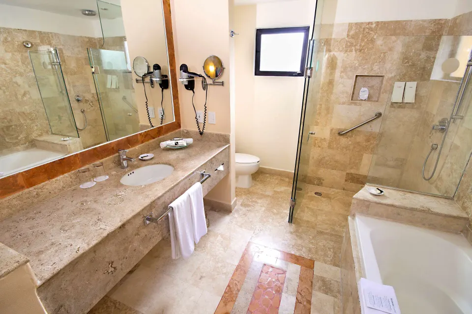 Deluxe room bathroom with vanity, tub and glass shower at Occidental Cozumel.
