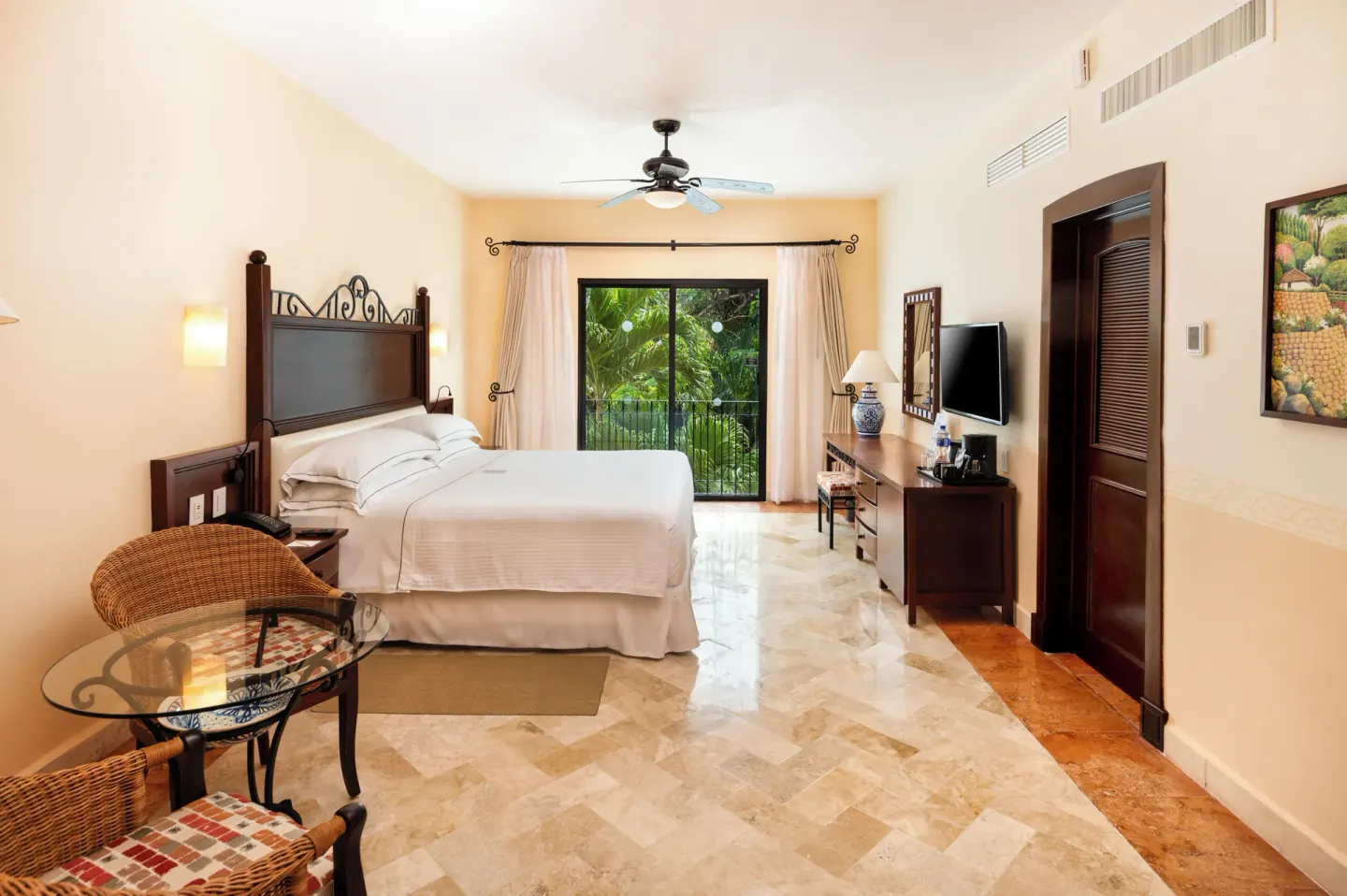 Deluxe room with king bed, seating area, TV and balcony greenery at Occidental Cozumel.
