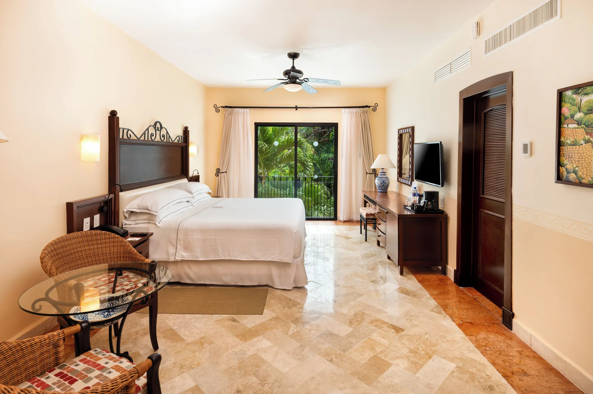 Deluxe room with king bed, seating area, TV and balcony greenery at Occidental Cozumel.