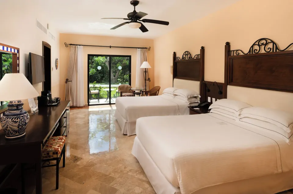 Deluxe room with two beds, dresser, seating nook and garden-facing doors at Occidental Cozumel.