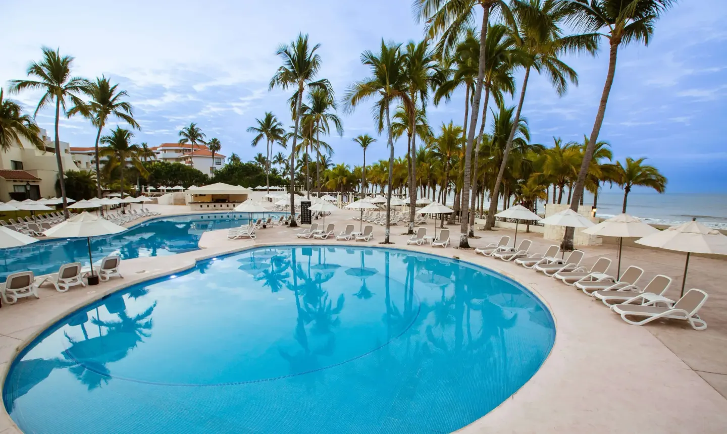 Curved pool with loungers, palms, and ocean beyond at Occidental Nuevo Vallarta.