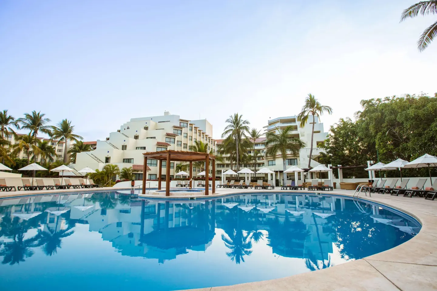 Curved pool with wooden pergola and shaded loungers at Occidental Nuevo Vallarta.
