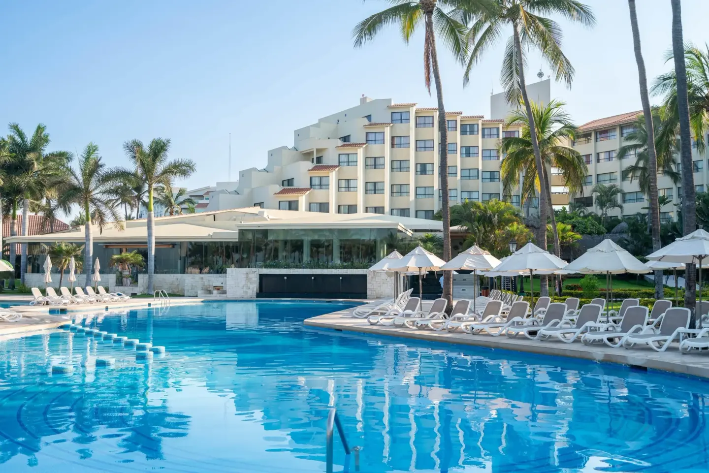 Main pool with loungers, umbrellas, palms, and resort building at Occidental Nuevo Vallarta.