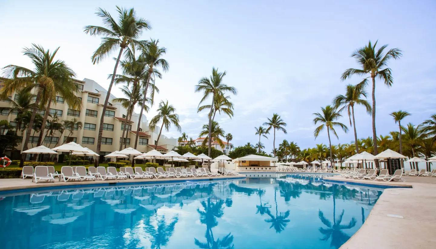 Long resort pool lined with loungers, umbrellas, and palm trees at Occidental Nuevo Vallarta.