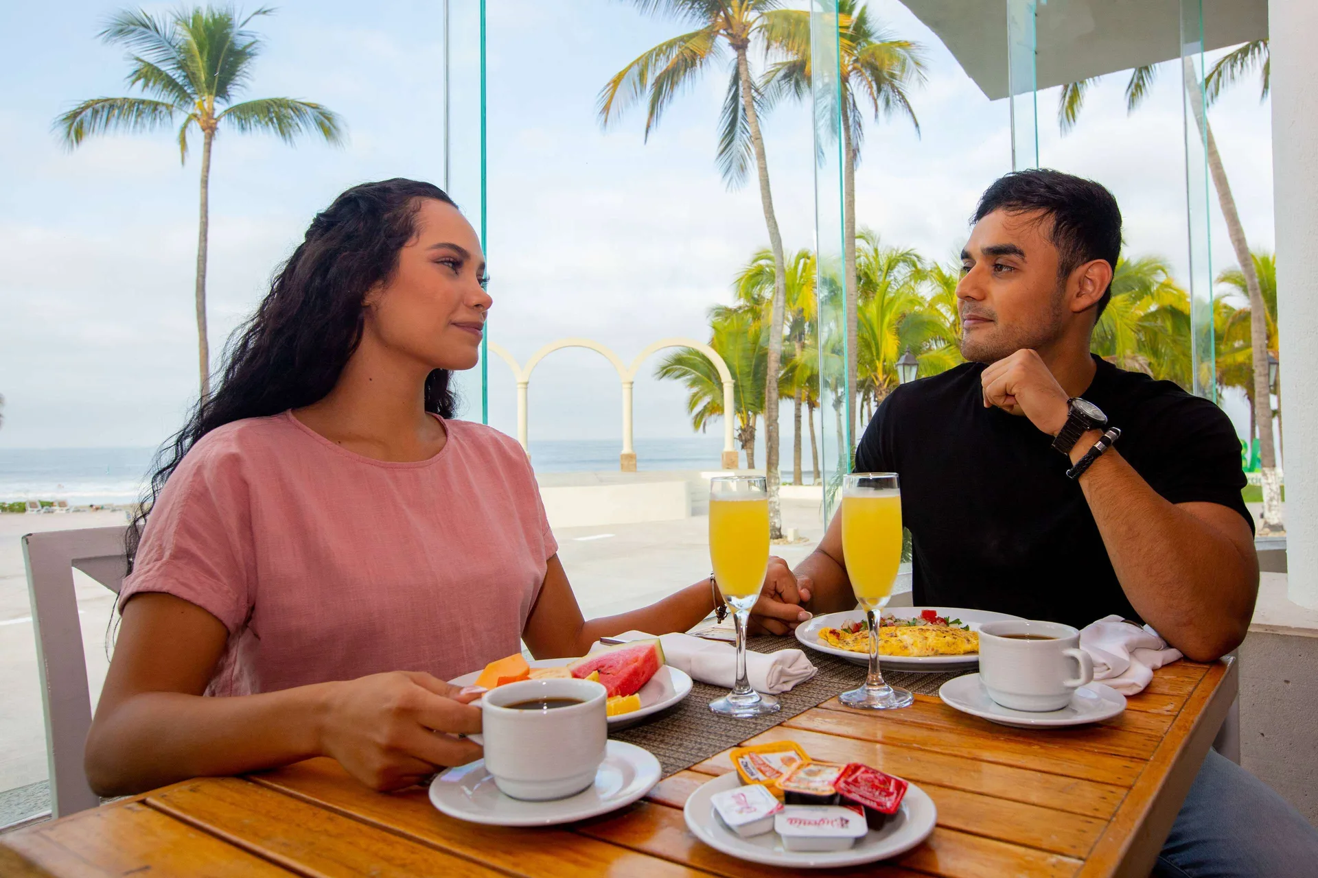Couple has breakfast by tall windows with palm and ocean views at Occidental Nuevo Vallarta.