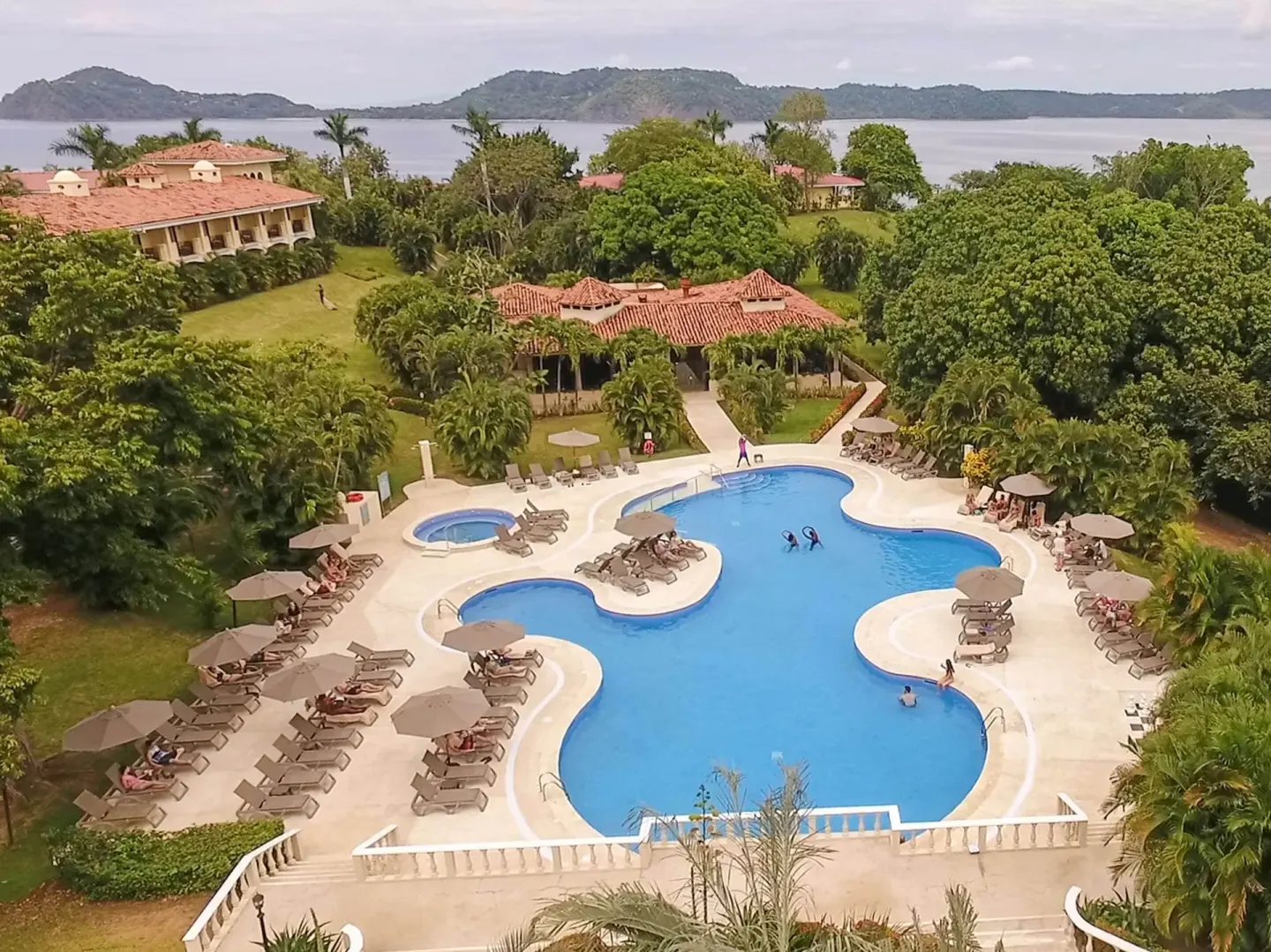 Aerial pool area with bay, gardens, and red-tile roofs at Occidental Papagayo.