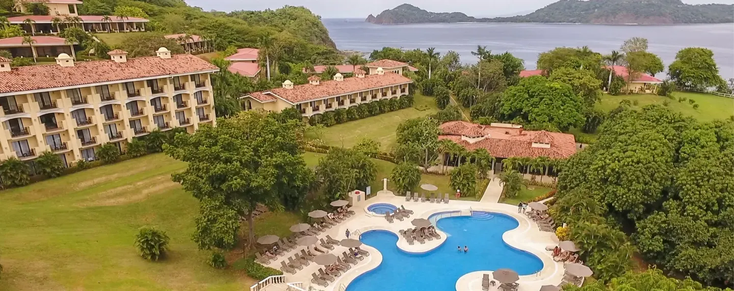Aerial view of pools, resort buildings, trees, and bay at Occidental Papagayo.