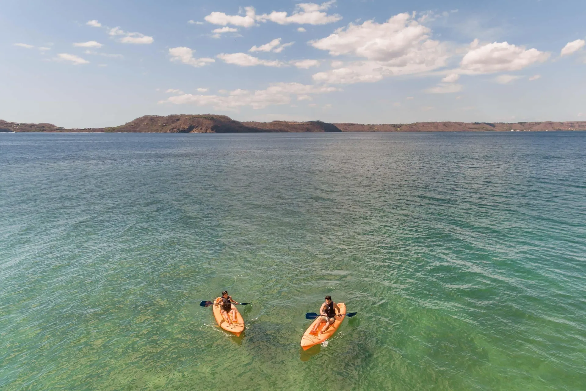 Two kayakers paddle over clear turquoise water near Occidental Papagayo.
