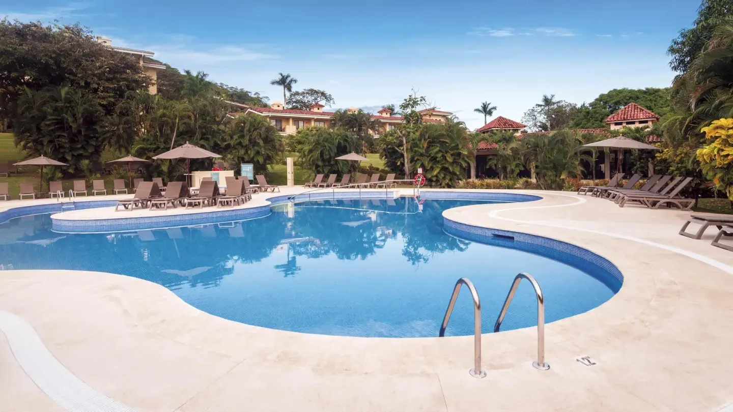 Large blue resort pool with ladders, loungers, and tropical gardens at Occidental Papagayo.