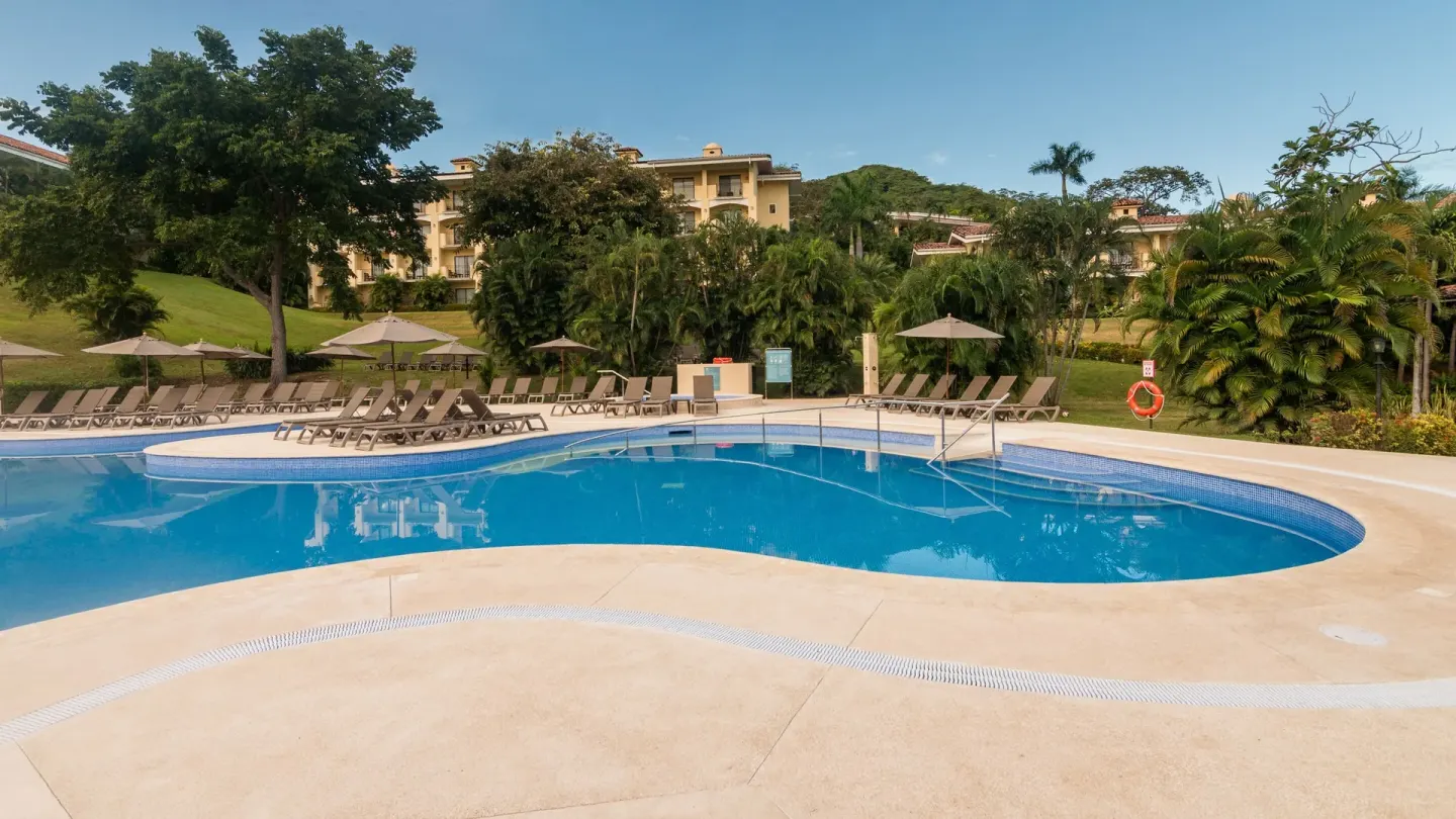 Pool deck with loungers, umbrellas, and garden buildings at Occidental Papagayo.