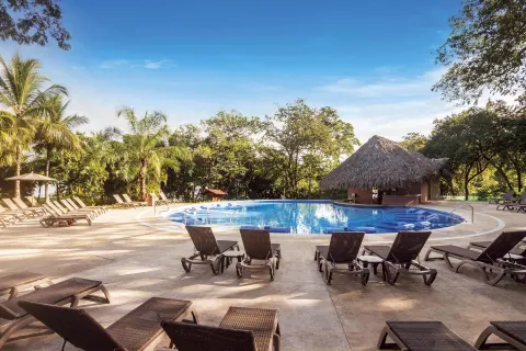 Pool deck with loungers, palms, and a thatched bar at Occidental Papagayo.