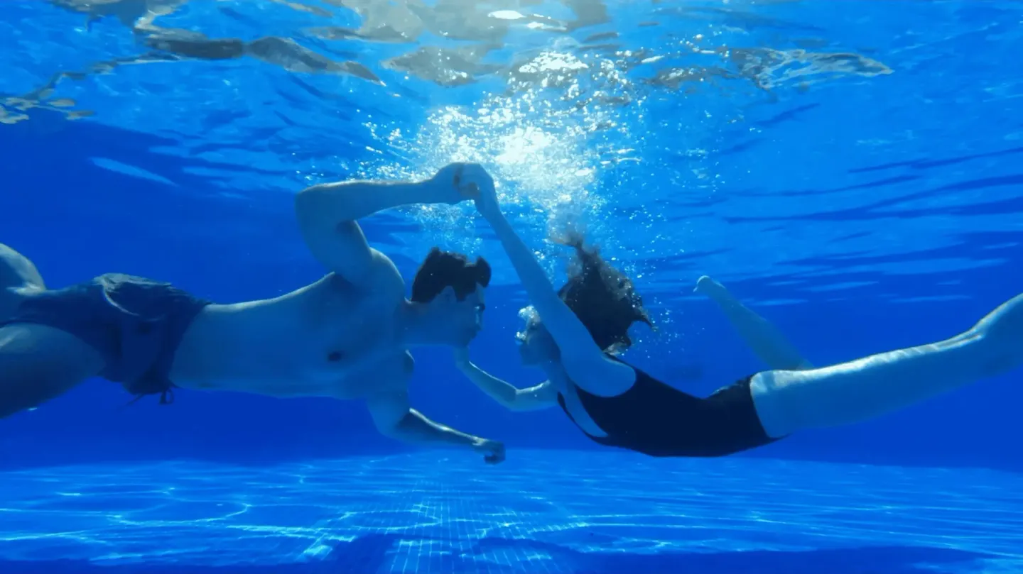 Two swimmers underwater in a blue pool at Occidental Papagayo.