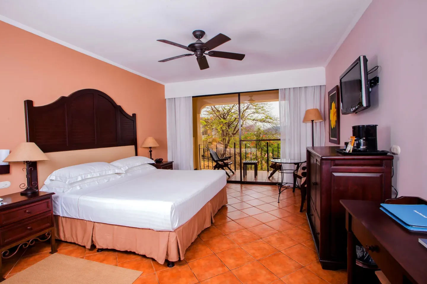 Deluxe Room king bed with balcony doors and wall-mounted TV at Occidental Papagayo.