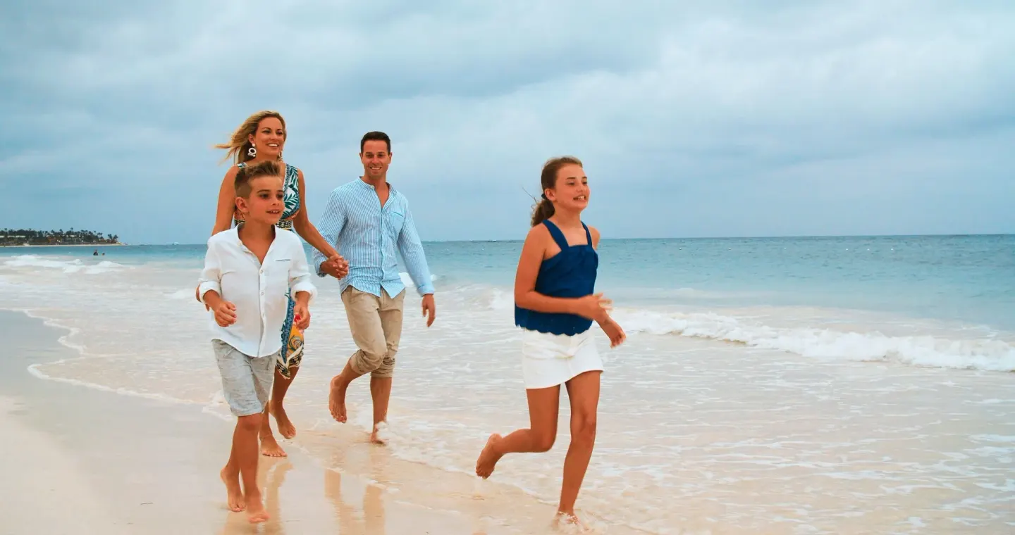 Family walking along the shoreline beside the ocean at Occidental Punta Cana.