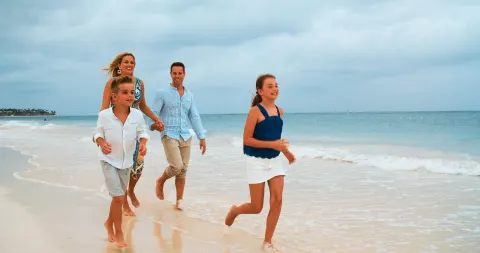 Family walking along the shoreline beside the ocean at Occidental Punta Cana.