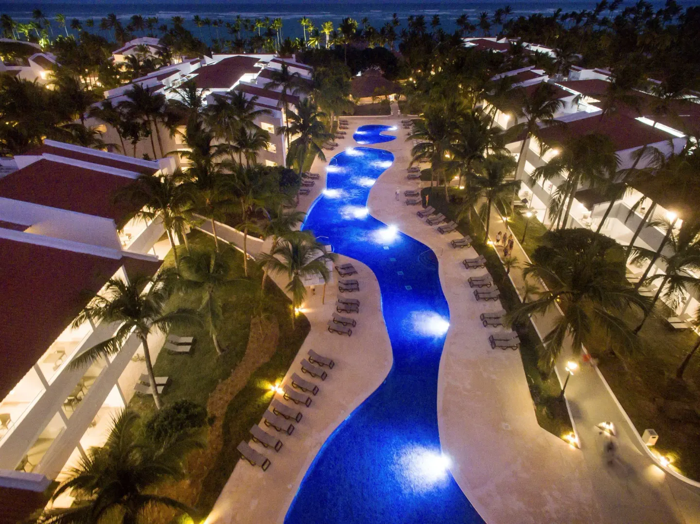 Night aerial view of an illuminated pool between resort buildings at Occidental Punta Cana.