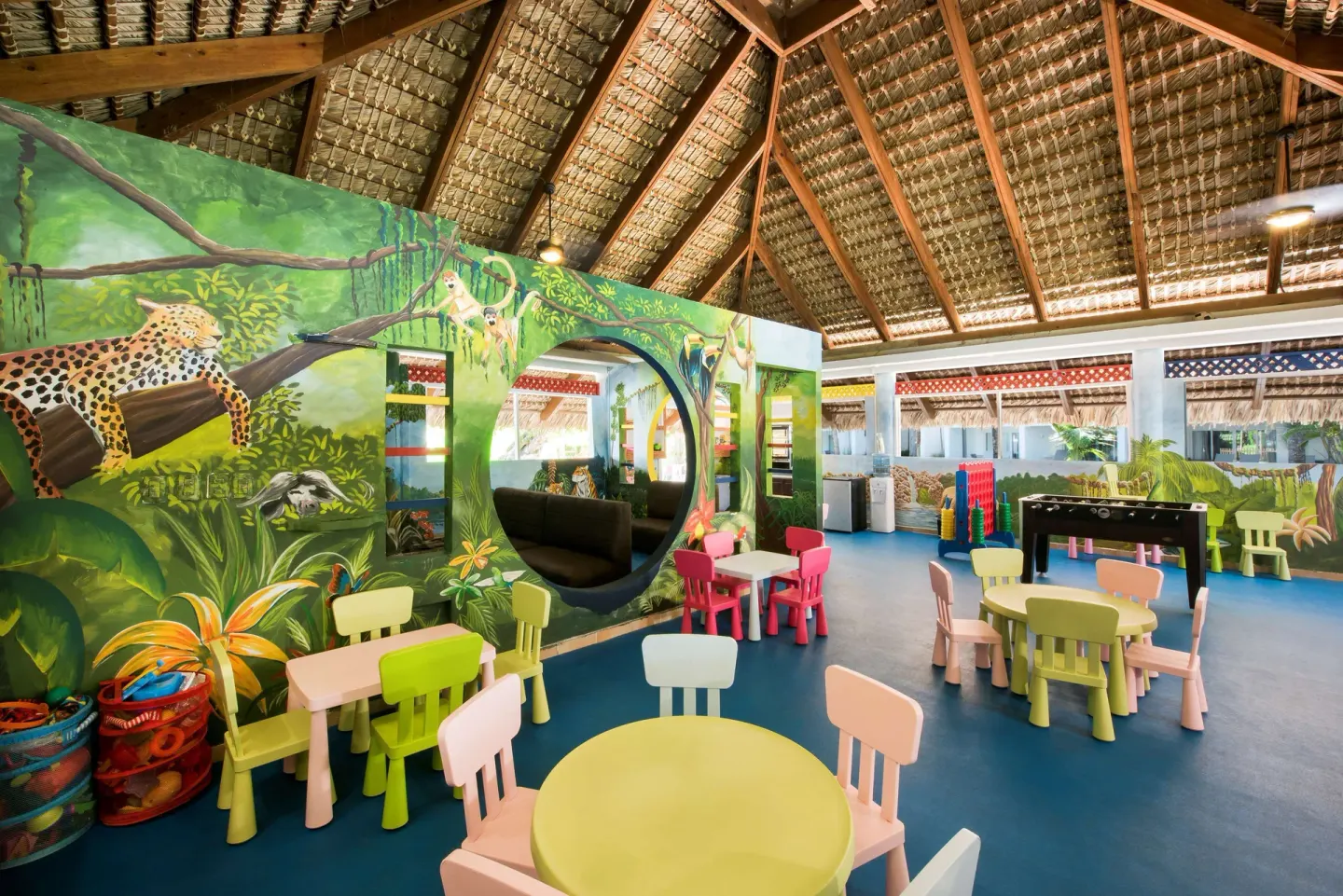Indoor kids' club with jungle mural, small tables, and foosball at Occidental Punta Cana.