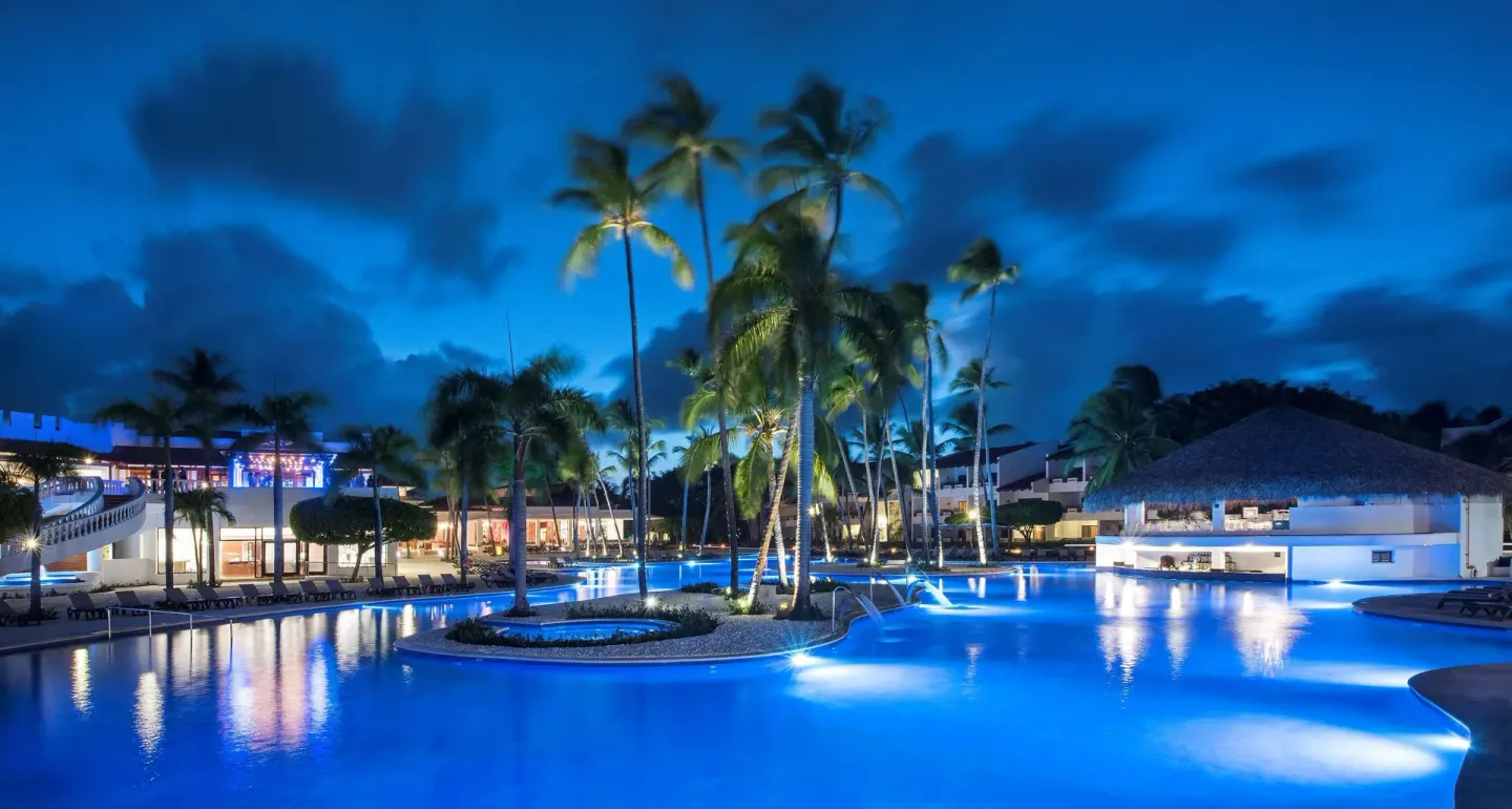 Blue-lit pool, palms, and a thatched-roof poolside structure at Occidental Punta Cana.