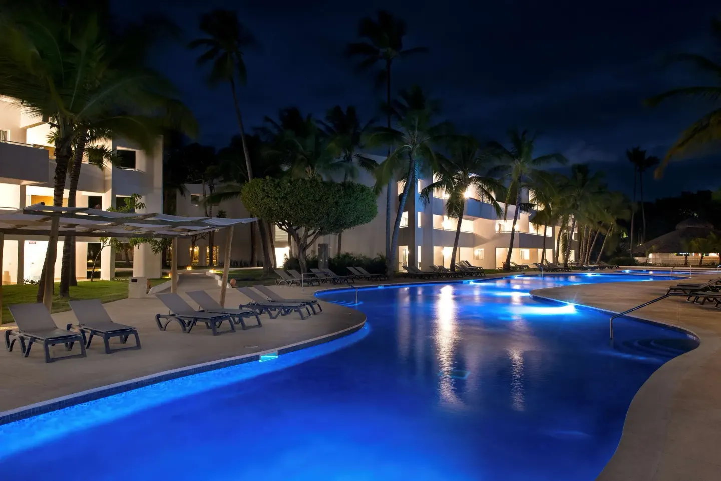 Illuminated resort pool at night with palms and loungers at Occidental Punta Cana.