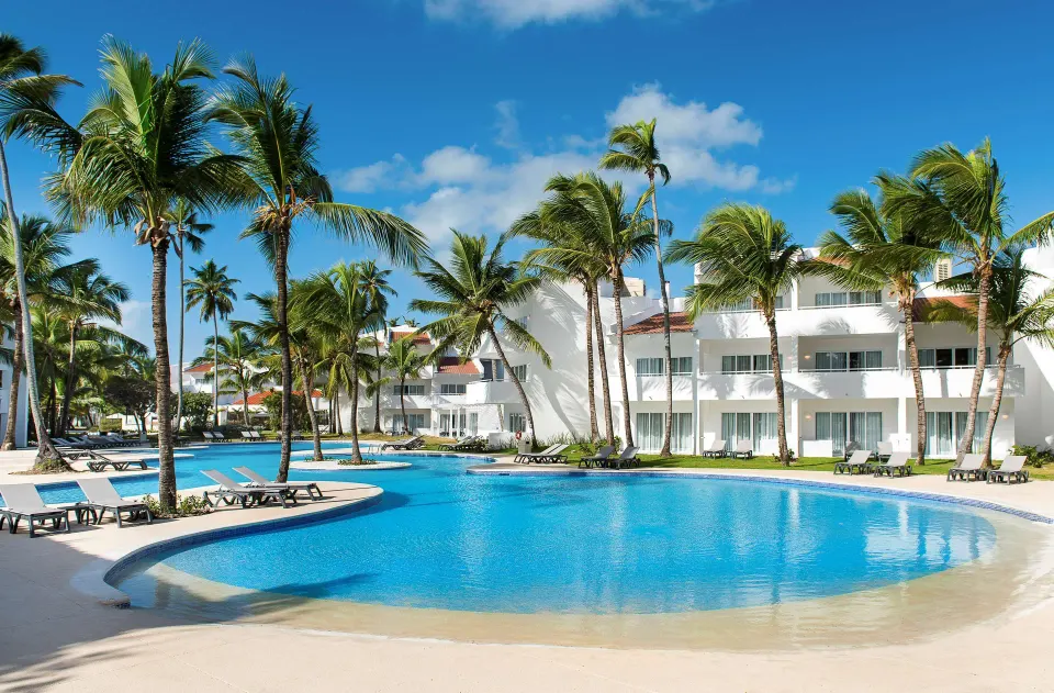 Curved swimming pool with palms and white guest buildings at Occidental Punta Cana.