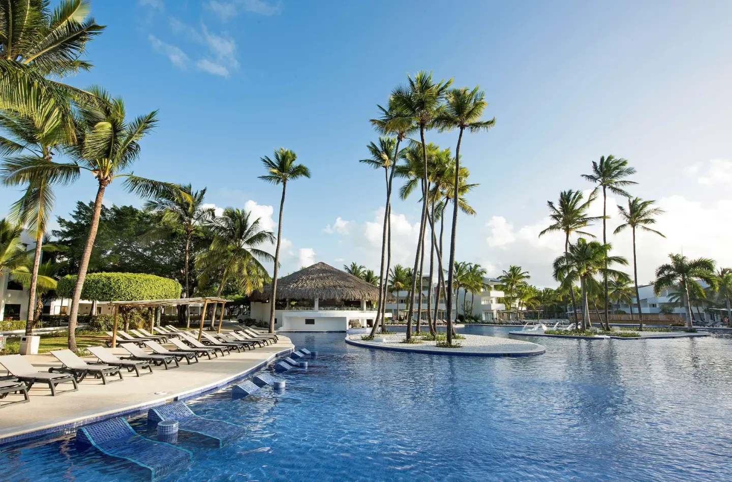 Pool with in-water loungers, palm islands, and rows of chairs at Occidental Punta Cana.