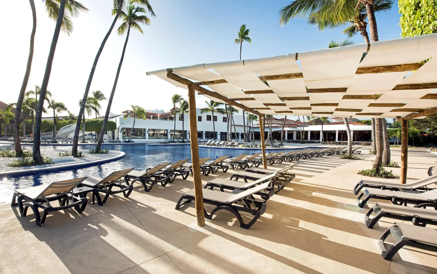 Poolside loungers under a shade pergola beside palms at Occidental Punta Cana.