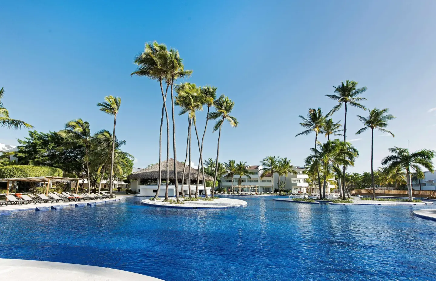 Wide blue pool with palm islands and resort buildings at Occidental Punta Cana.