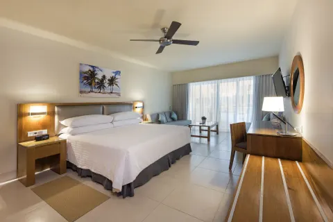 Superior Room with king bed, desk, sofa and balcony light at Occidental Punta Cana.