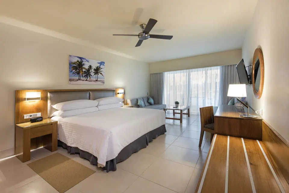 Superior Room with king bed, desk, sofa and balcony light at Occidental Punta Cana.