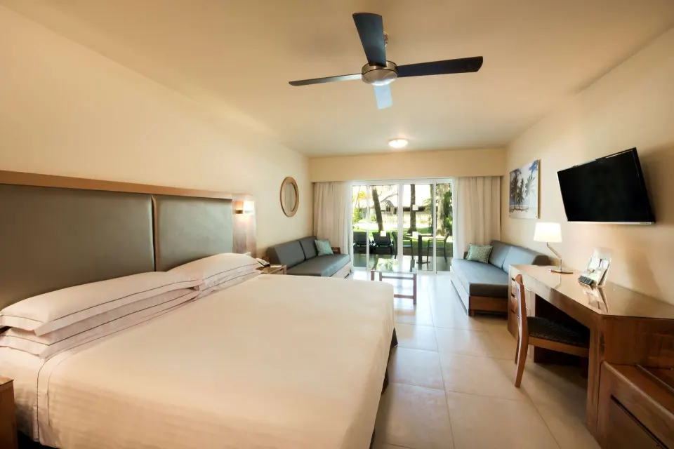 Superior Room king bed with sofas, desk, TV, and patio view at Occidental Punta Cana.