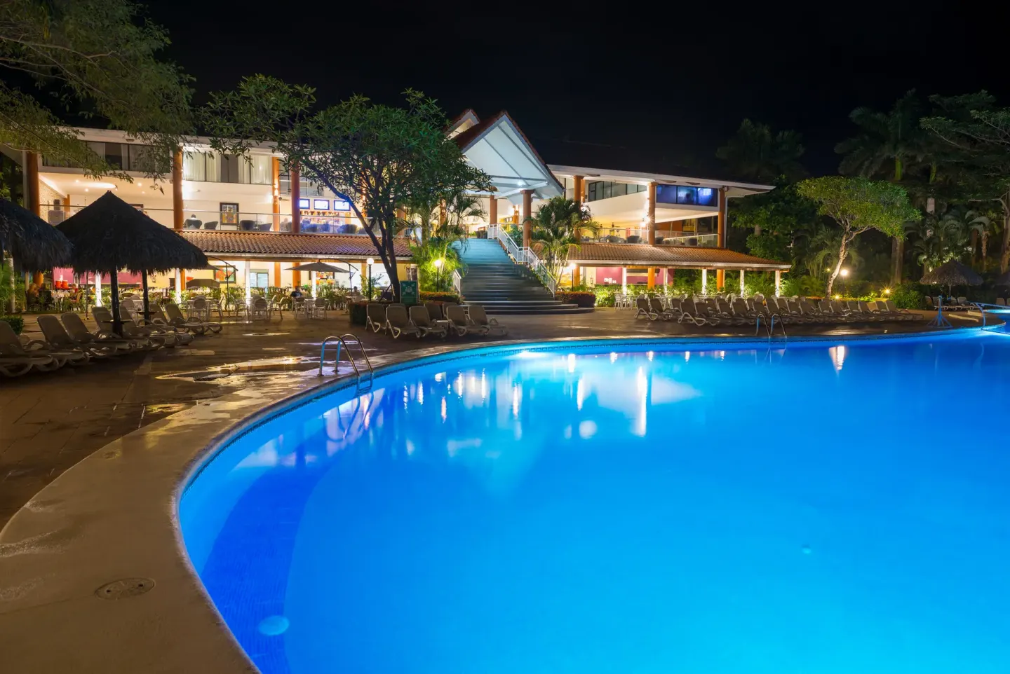 Curved blue pool and lit resort building at night at Occidental Tamarindo.