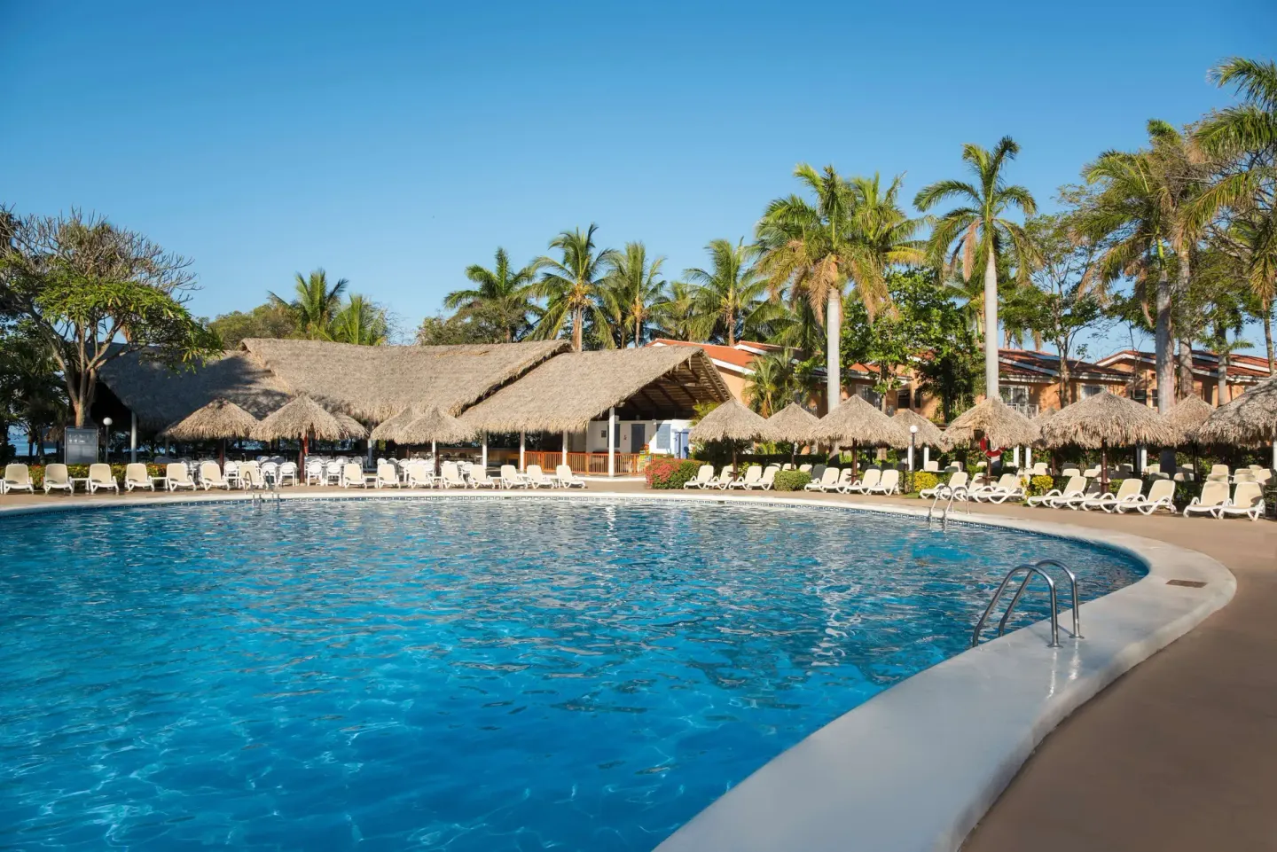 Curved pool with lounge chairs and thatched roofs at Occidental Tamarindo.