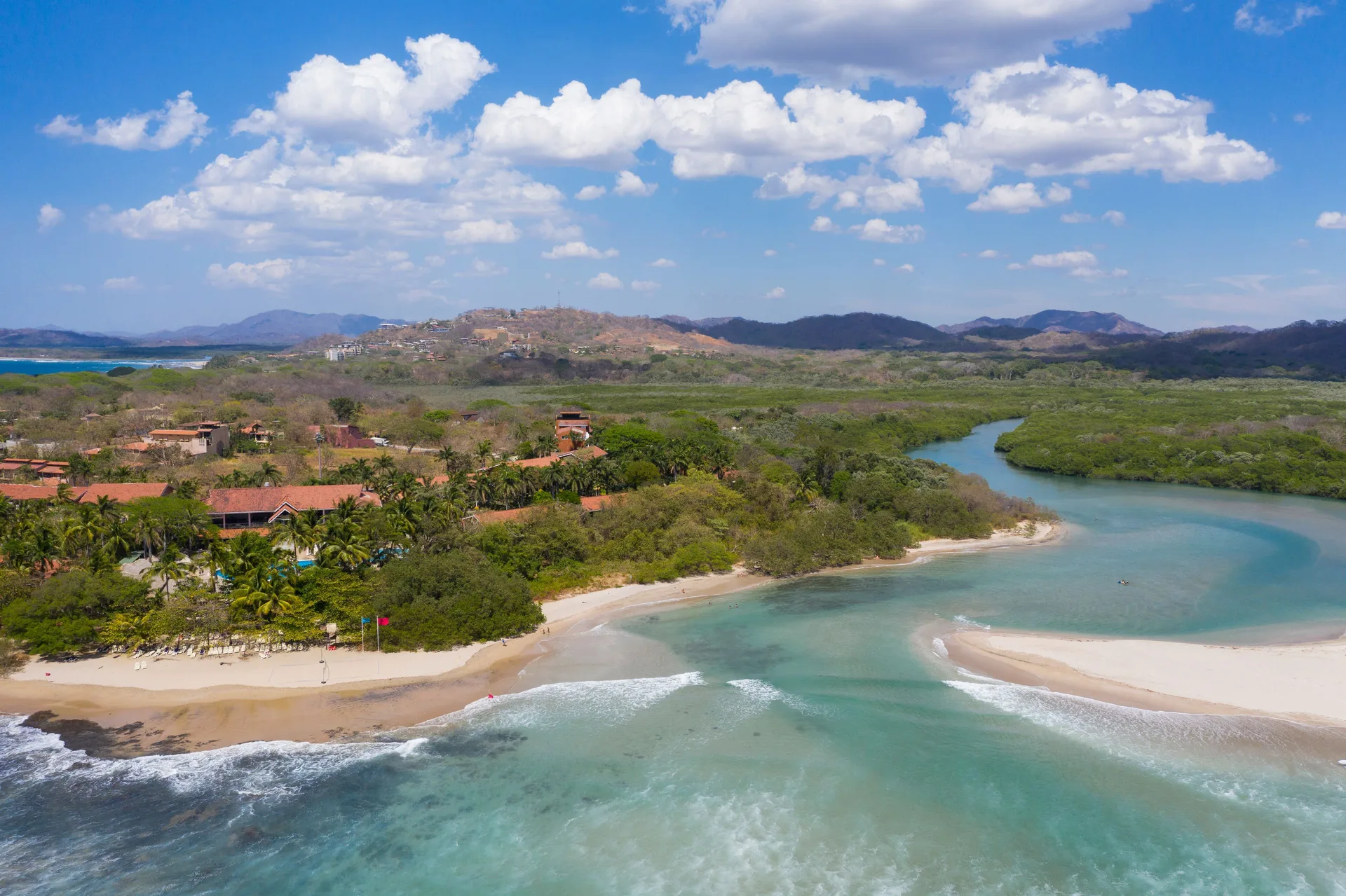 Aerial view near Occidental Tamarindo showing beach, river mouth, green estuary, and hills.