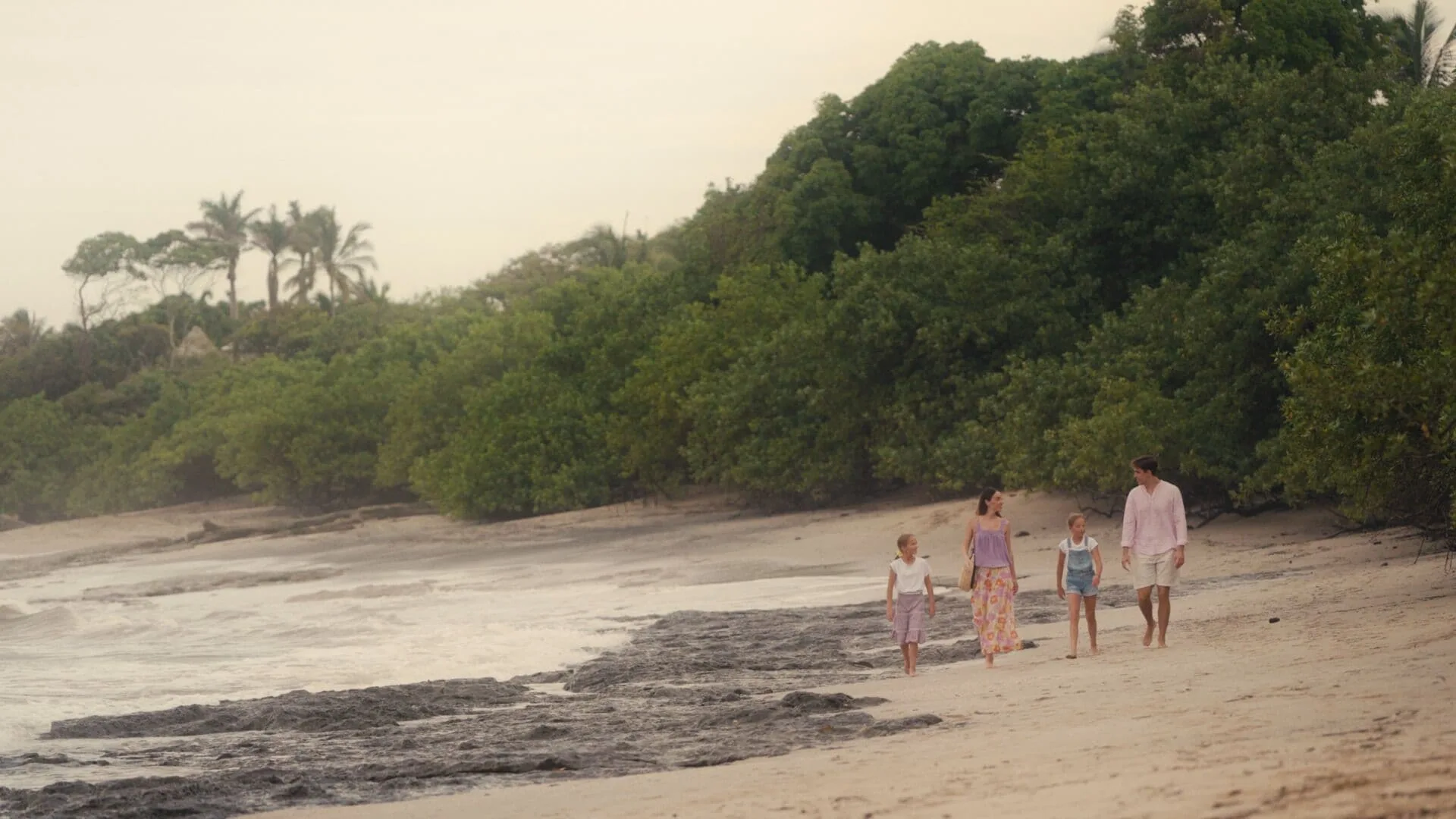 A family walks along a rocky, tree-lined beach near Occidental Tamarindo.