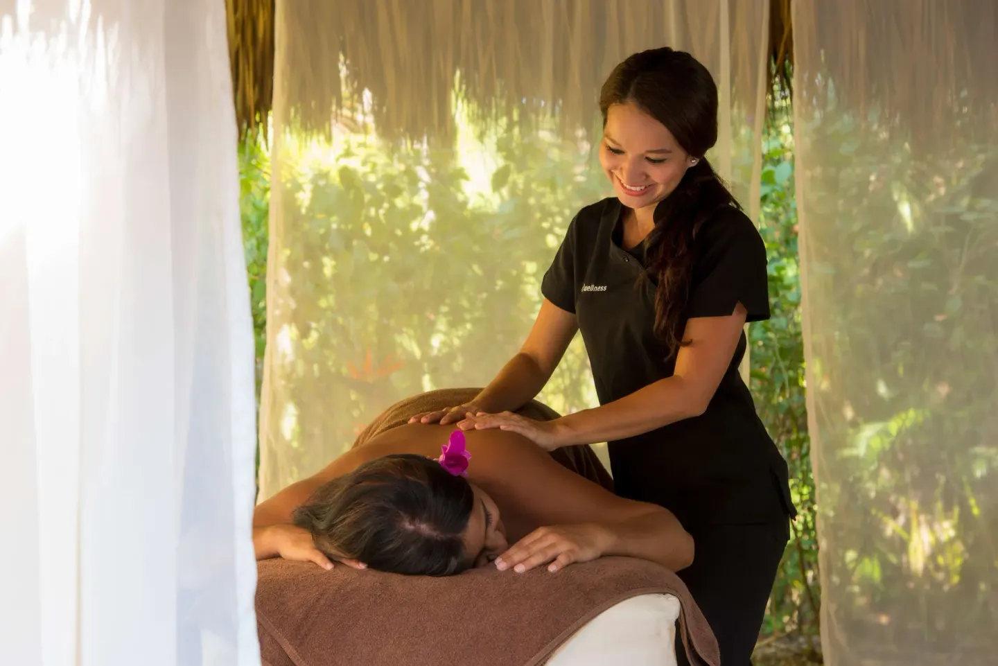 Spa therapist giving a massage in a curtained garden cabana at Occidental Tamarindo.