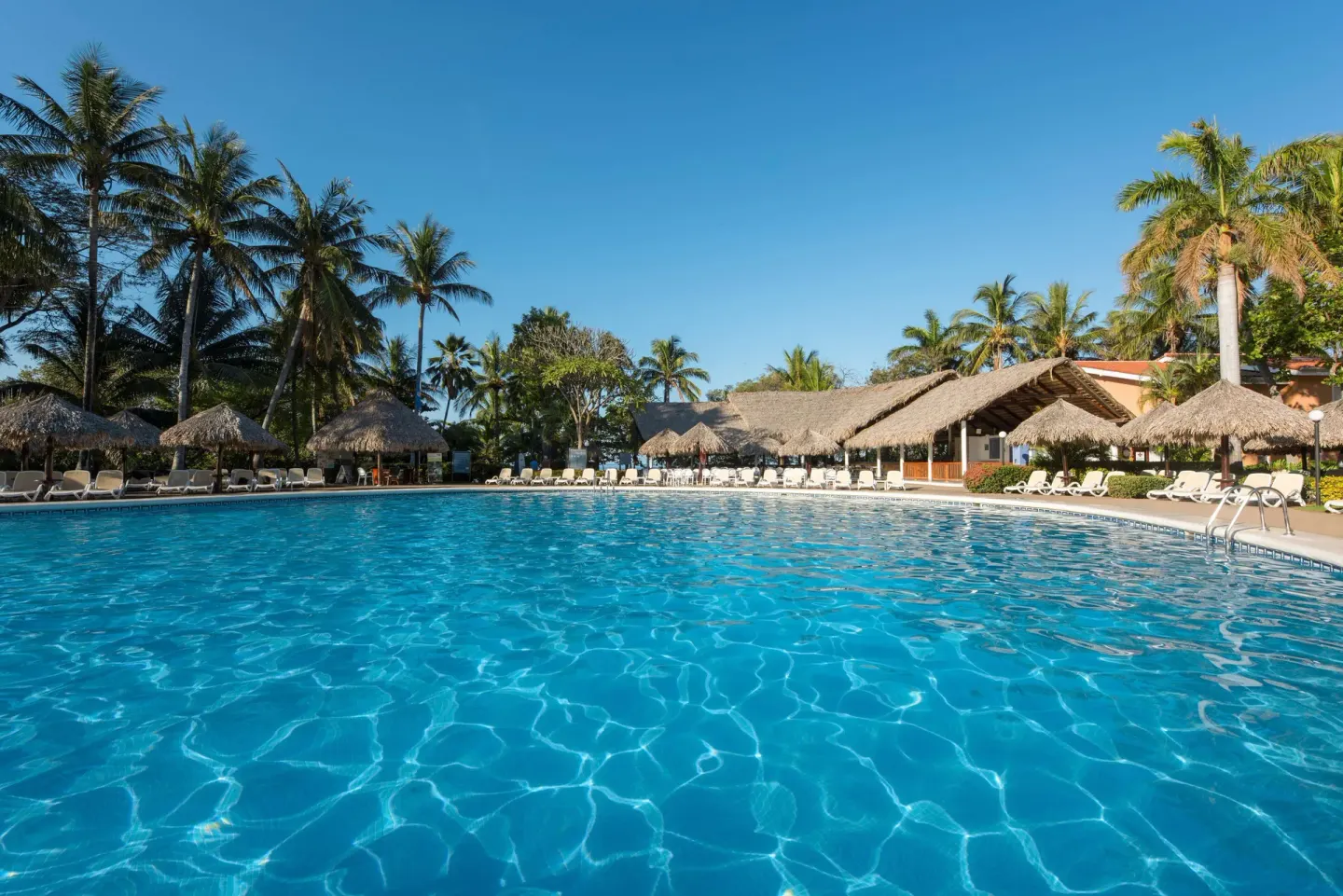 Blue swimming pool bordered by palms and palapas at Occidental Tamarindo.