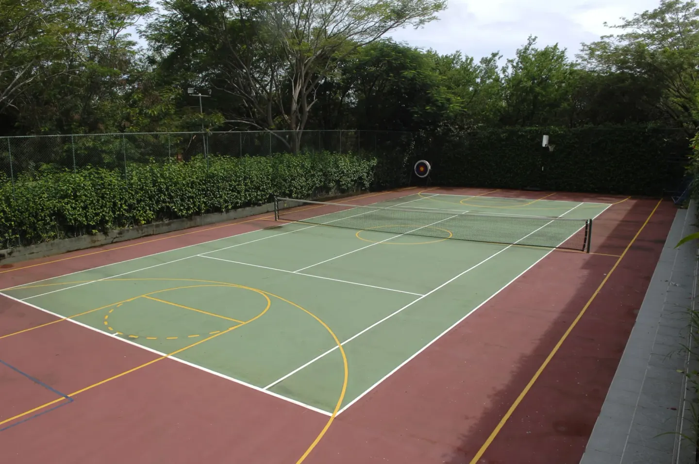 Outdoor tennis court surrounded by hedges and trees at Occidental Tamarindo.