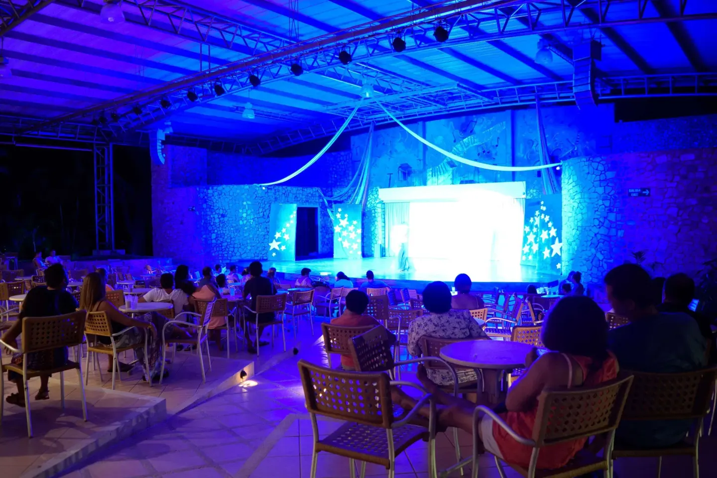 Audience seated at tables watching a brightly lit stage show at Occidental Tamarindo.