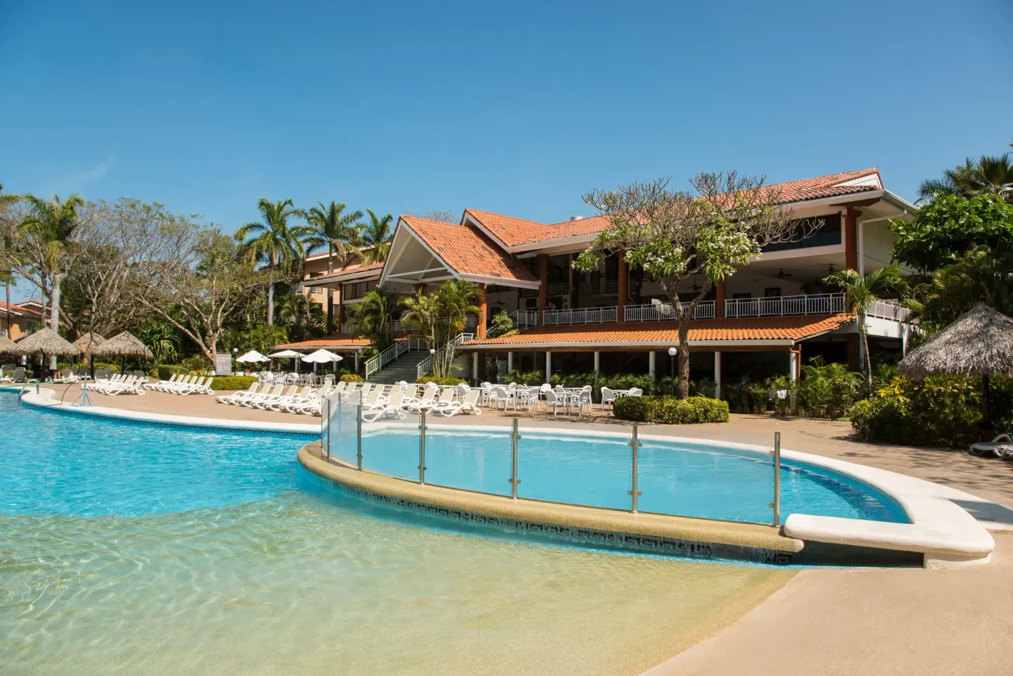 Shallow pool area with glass railing and resort building at Occidental Tamarindo.