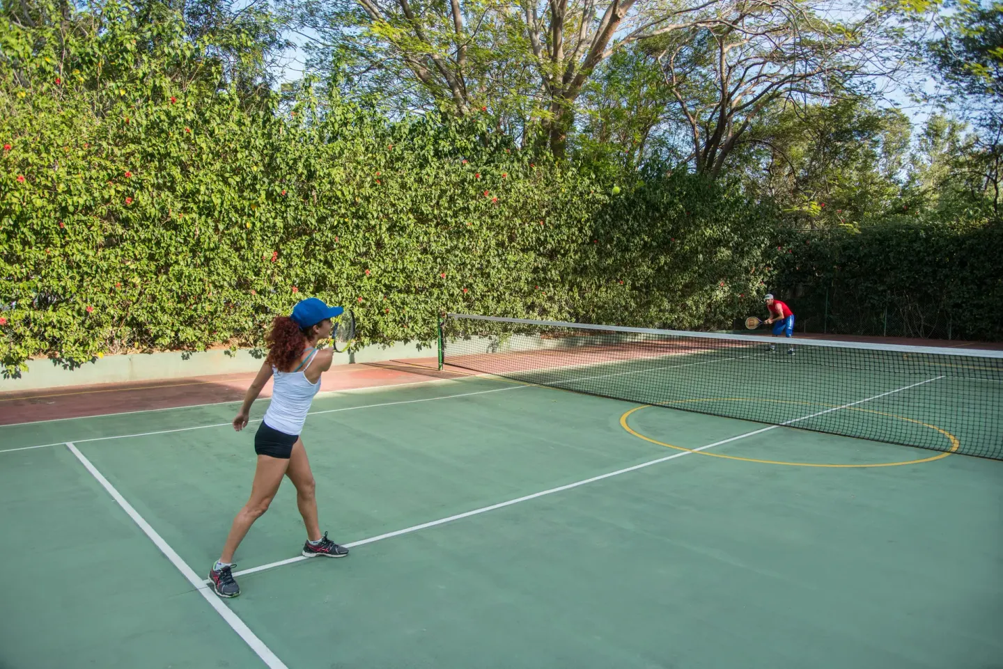 Two guests play tennis on a green court at Occidental Tamarindo.