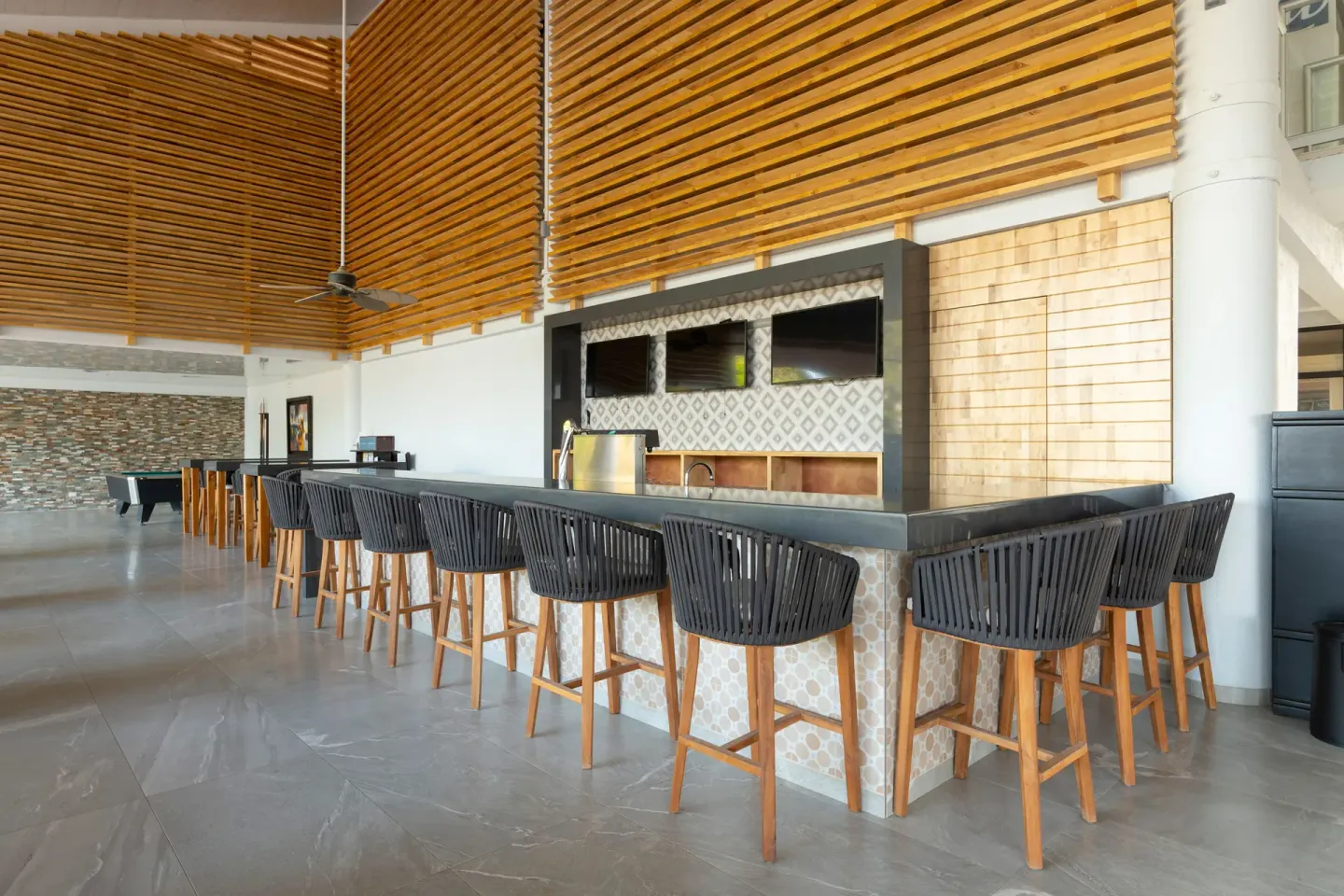 Long indoor bar with stools and wall screens at Occidental Tamarindo.