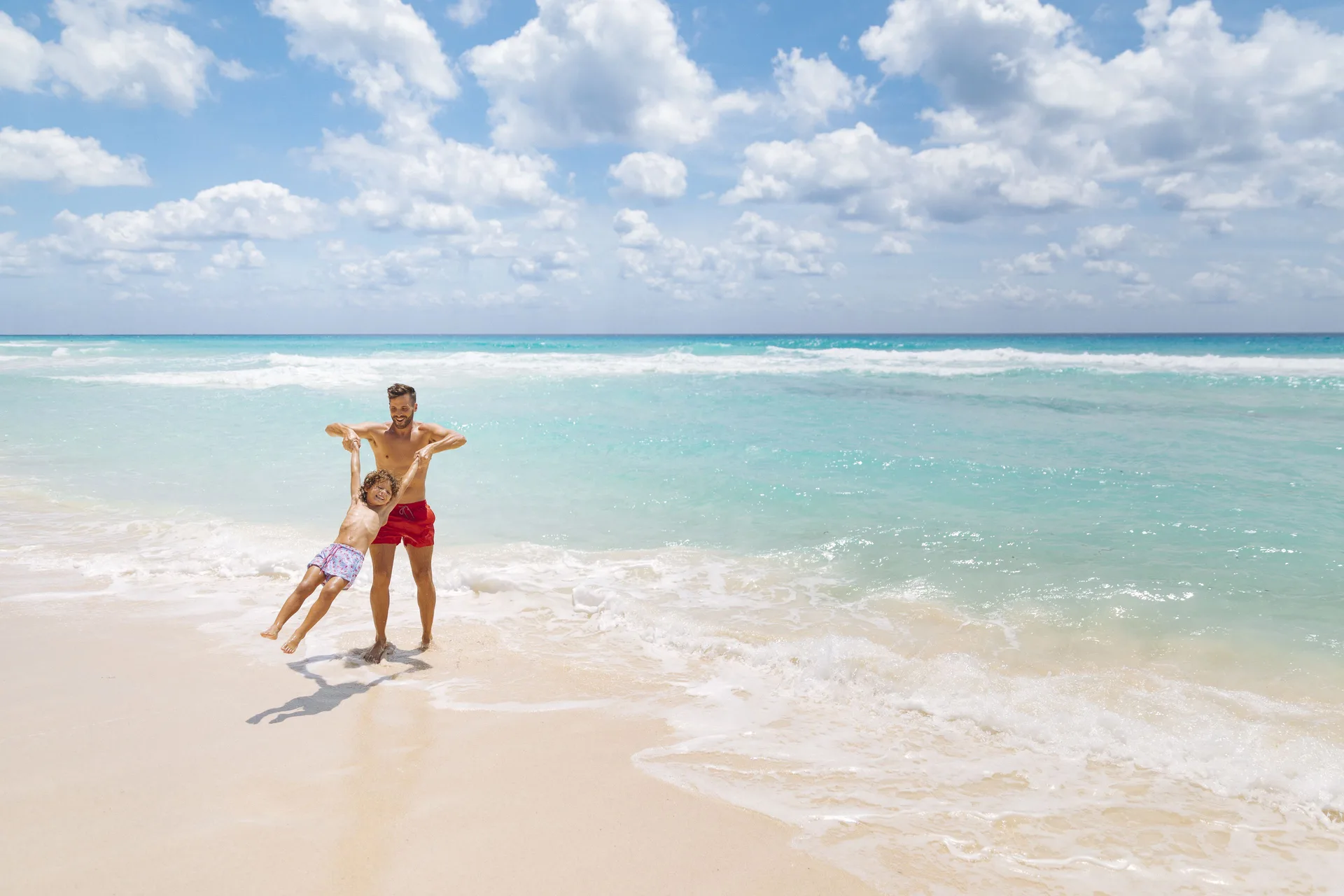A man and child play in the surf on the beach at Occidental Tucancún.