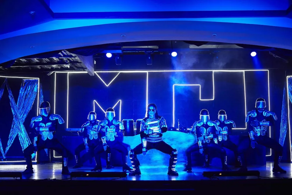 Blue-lit performers in futuristic costumes on stage at Occidental Tucancún.