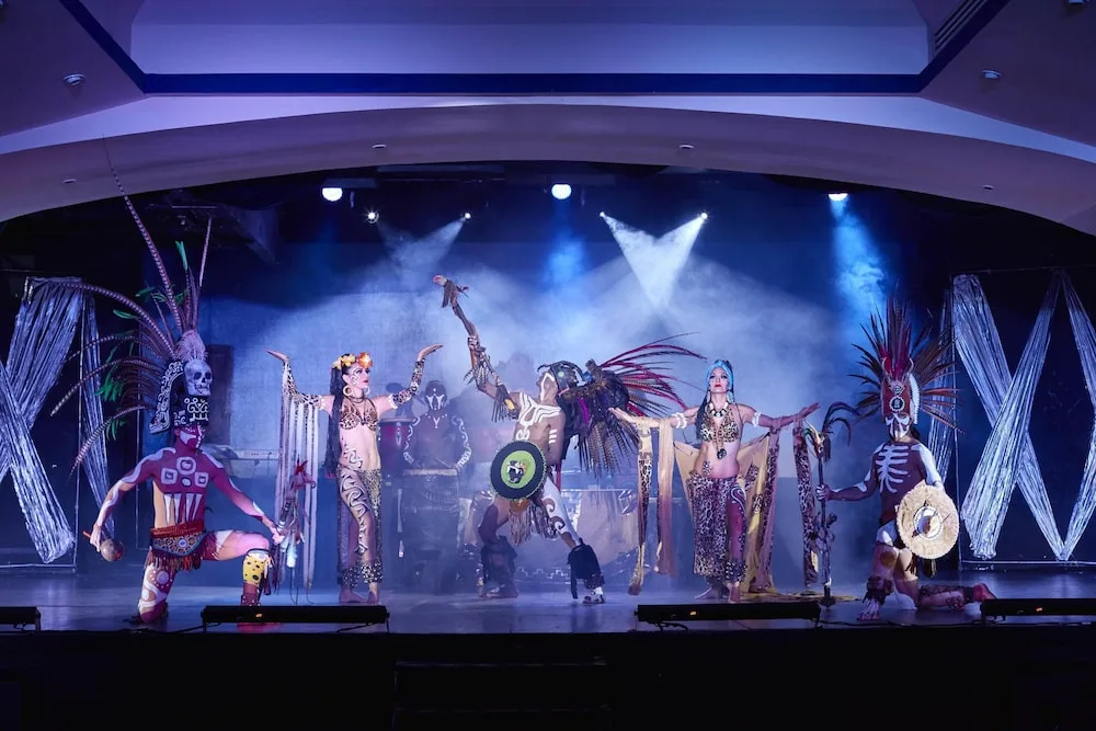 Costumed dancers perform on a lit indoor stage at Occidental Tucancún.