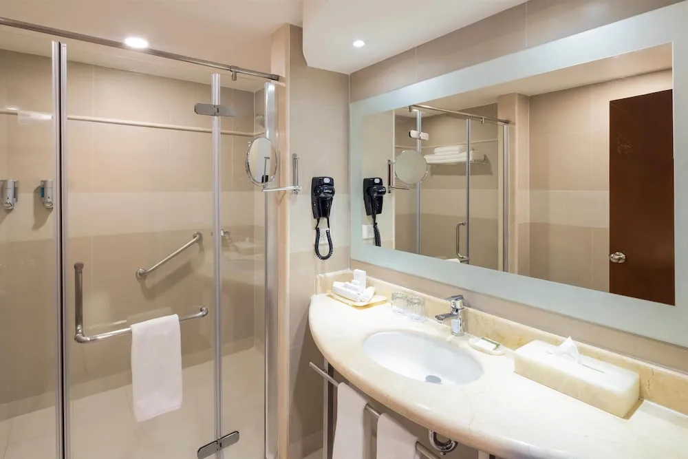 Bathroom with glass shower, sink, mirror, and towels at Occidental Tucancún.
