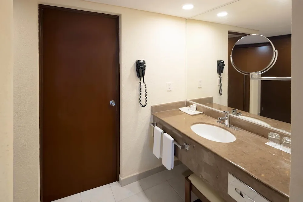 Bathroom vanity with sink, mirror, hair dryer, and towels at Occidental Tucancún.