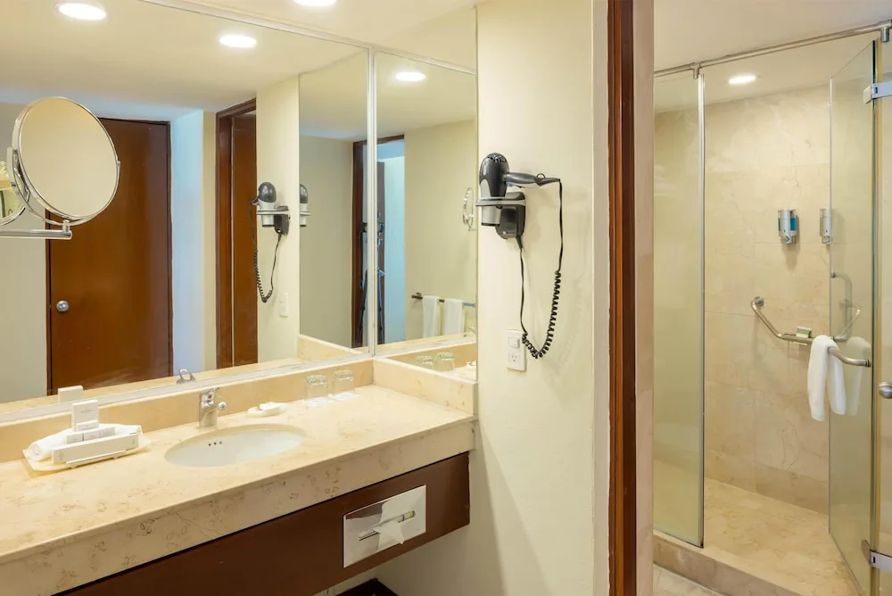 Bathroom vanity and glass shower with wall-mounted hair dryer at Occidental Tucancún.