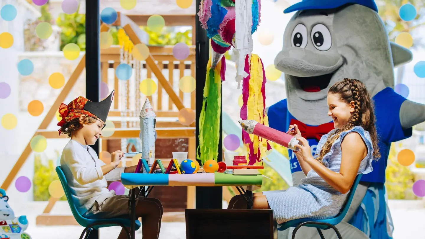 Children doing crafts beside a dolphin mascot in the kids club at Occidental Tucancún.