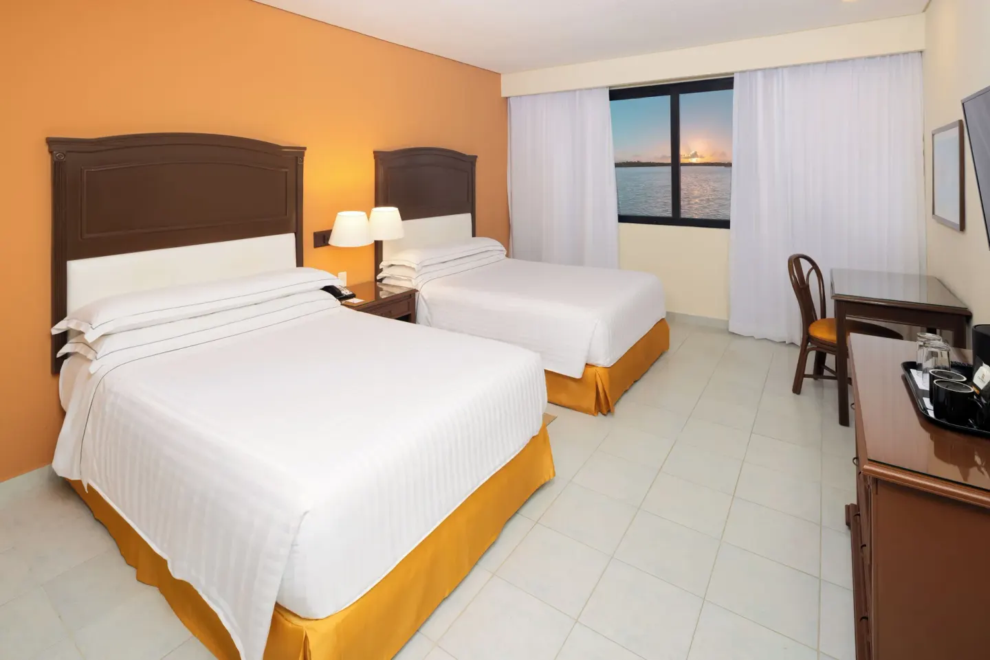 Two-bed guest room with lagoon-view window at sunset at Occidental Tucancún.