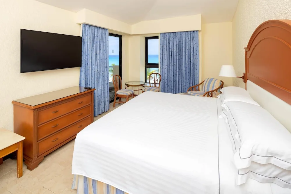 King guest room with TV, blue curtains and ocean glimpses at Occidental Tucancún.